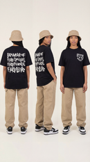 Three Black women wearing the LOVEUS "Beware of Fake" black graphic t-shirts, styled with braids and bucket hats against a white background.