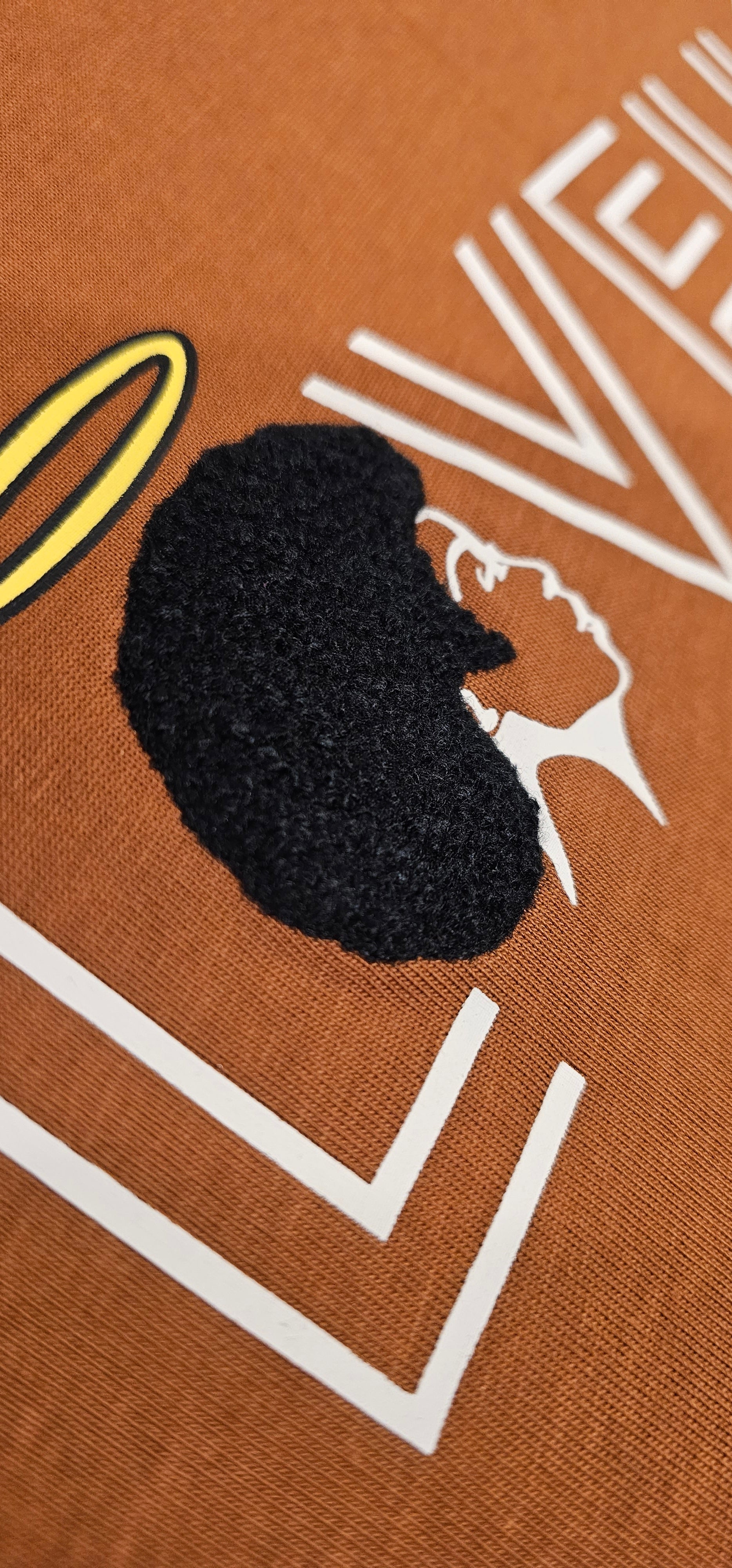 A detailed close-up shot of the Caramel Angel tee, highlighting the intricate, raised embroidered textures that beautifully mimic natural hair.