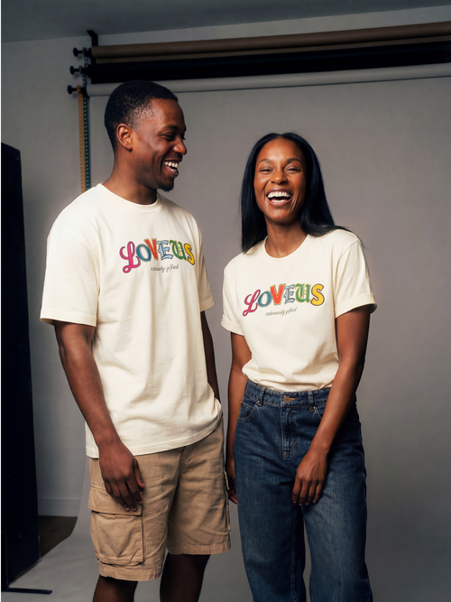 Two people laughing side by side against a plain studio background, wearing the relaxed-fit Extremely Gifted Heavyweight Graphic Tee to showcase its abstract letterform design.