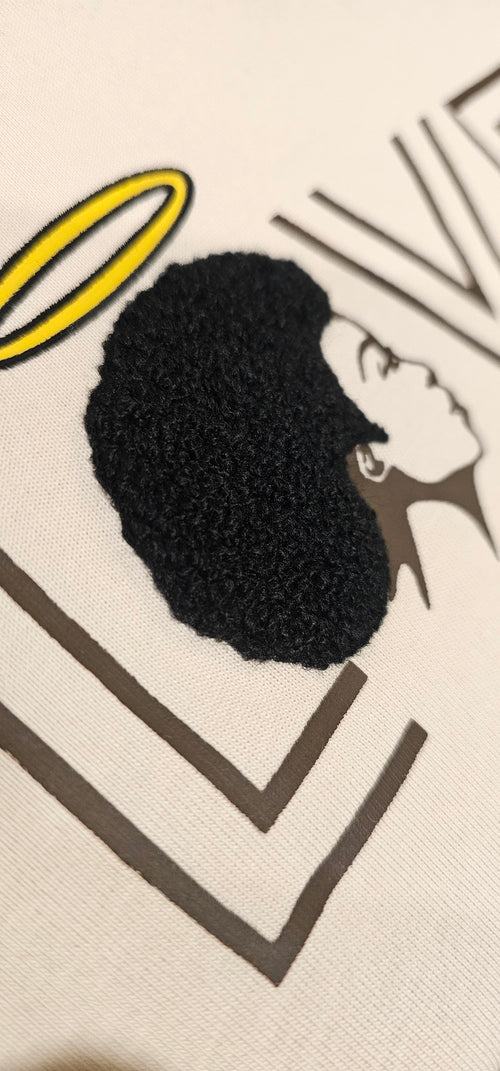 A detailed close-up of the Ivory Angel cotton shirt showcasing the intricate, raised embroidered afro design mimicking natural hair texture.