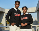 A Black man and a Black woman confidently posing together outdoors in formal clothing, showcasing the black Loveus We Are Dope Cursive Rugby Polo with its distinct white collar.