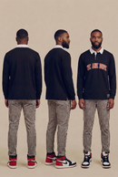 Three studio views of a man wearing the black We Are Dope Heavyweight Rugby Polo with bold red and white text detailing, paired with checkered pants against a beige background.